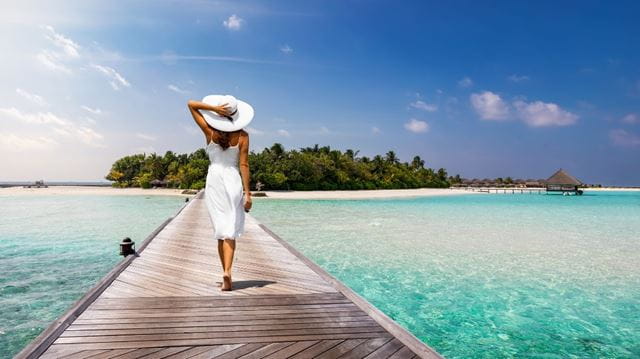 Woman wearing a white dress with sun hat on the beach